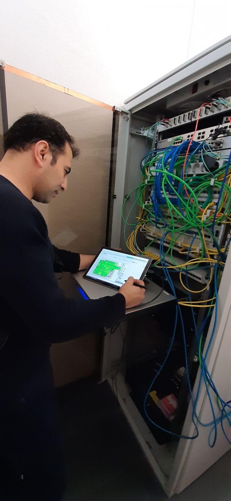 Mirwaiss Ghafari prüft am Netzwerkschrank eine WLAN-Ausleuchtung auf dem Tablet